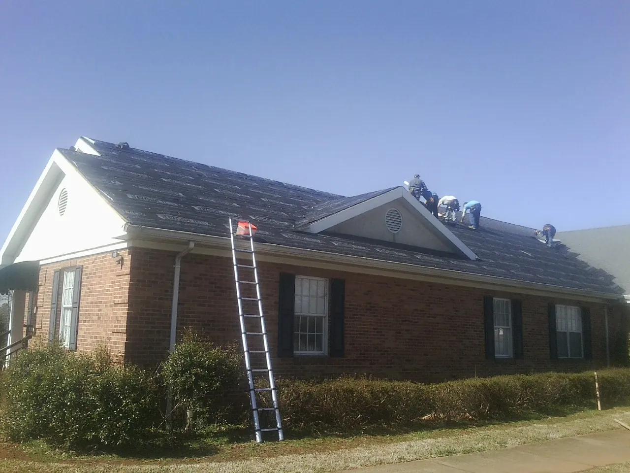 Crew tearing shingles off a brick ranch roof with a ladder set — Emergency Roof Repair work by our crew in Alder