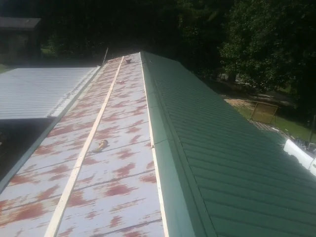 Old rusted panels beside newly installed green metal roofing — Wind Damage Roof Repair by Roofing Brothers in Alder