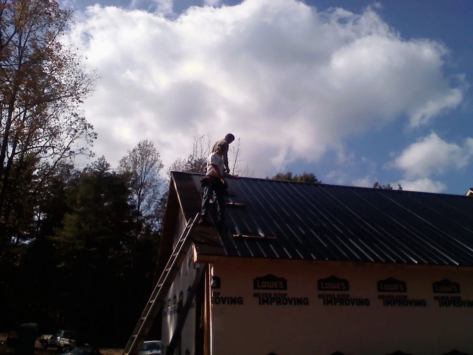 Roofer fastening dark metal panels high against a cloudy sky, from a Roof Inspection job in Alder